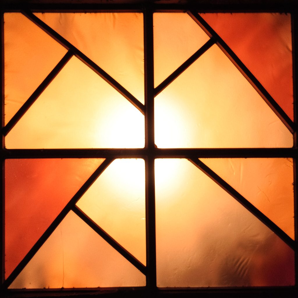 Stained-glass composition with interlocking shapes in olive green, rose, and cream, separated by strong dark lead lines.