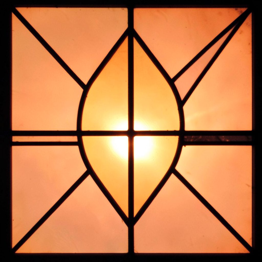 A stained-glass panel in layered greens and blush pinks, with bold dark leading forming geometric segments.